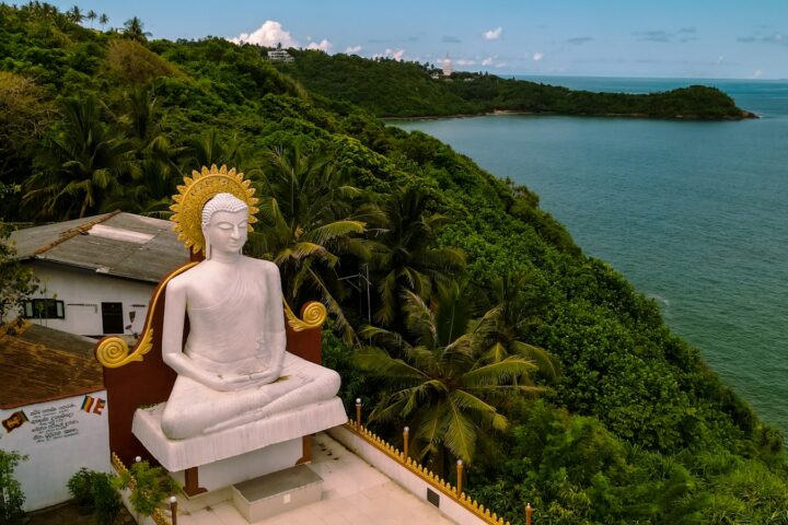 a statue of a person sitting on a bench by a body of water