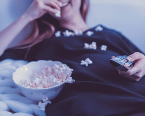 woman lying on bed while eating puff corn